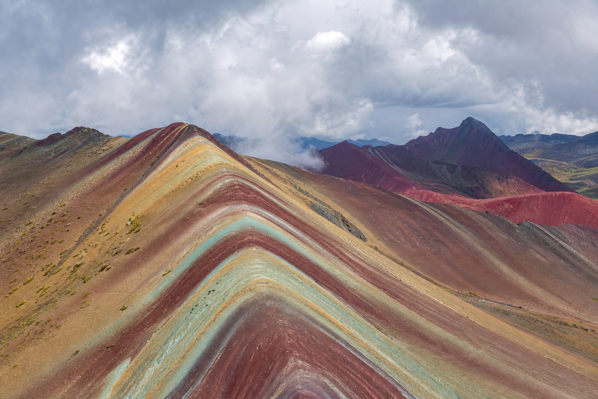 Hikers on the striped mineral ridges of Rainbow Mountain (Vinicunca) with the snow-capped Vilcanota range behind them
